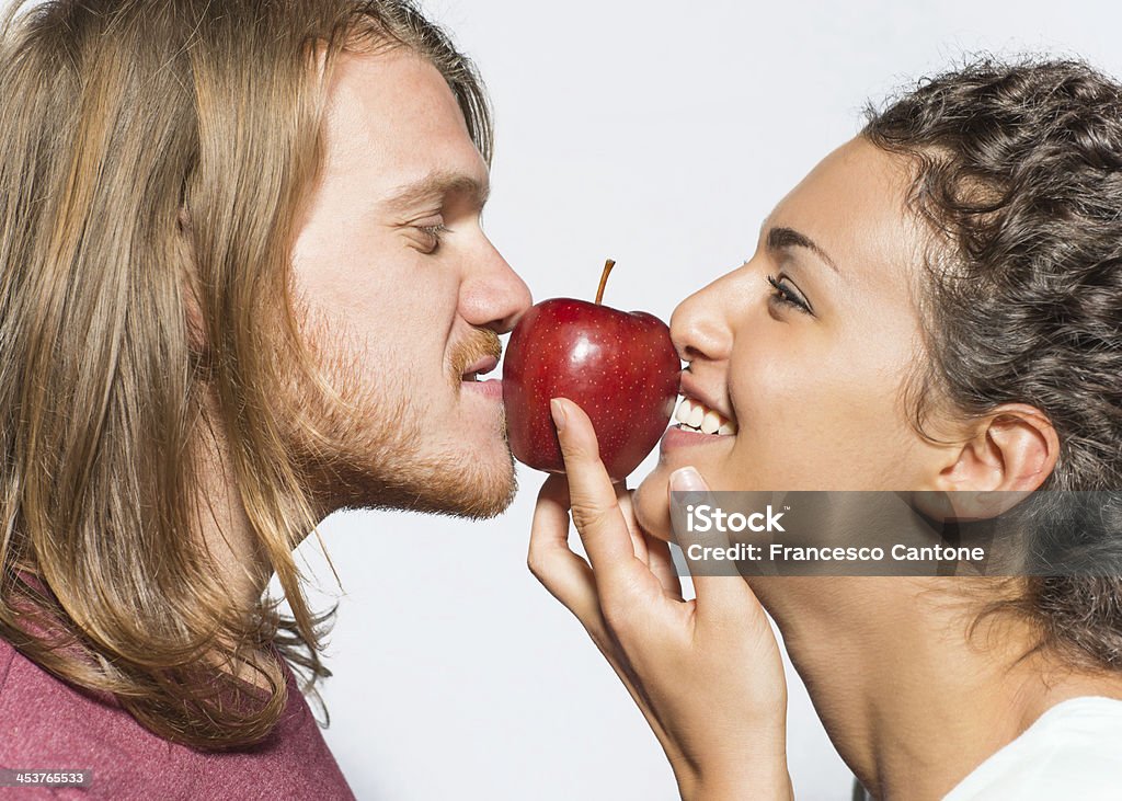 Boy and girl kiss an apple A Boy and a girl kiss a red apple on a light grey background and smile. Apple - Fruit Stock Photo