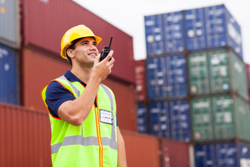 young harbor worker talking on the walkie-talkie at container warehouse