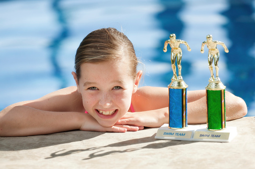 Subject: Portrait of young girl  competitive swimmer with her trophies by the swimming pool.