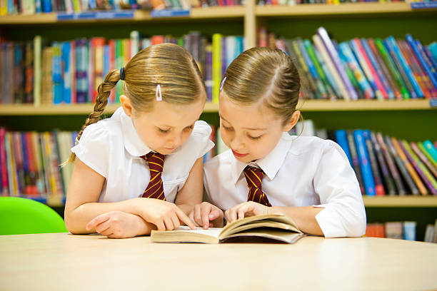 Two young girls in uniform reading a book in a library stock photo