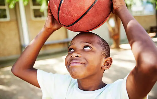 Cute young African American boy standing outdoors holding a basketball above his head