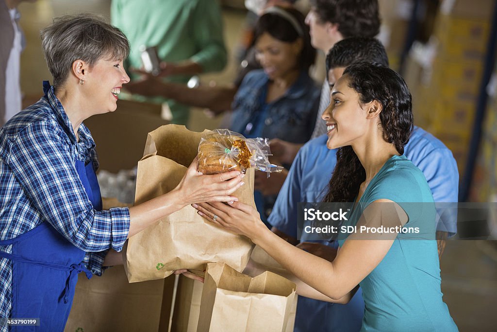 Girl handing a bag of food to a woman in an apron People standing in line to donate food for disaster relief Food Stock Photo