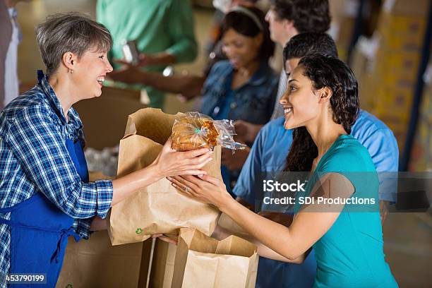 Girl Handing A Bag Of Food To A Woman In An Apron Stock Photo - Download Image Now - Food, People, Waiting In Line