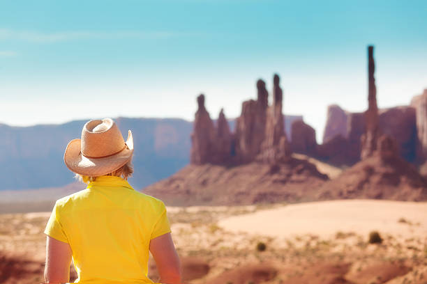 Subject: Tourist cowgirl sightseeing, viewing the Totem Pole rock formations in Monument Valley, a landmark of the American Southwest.