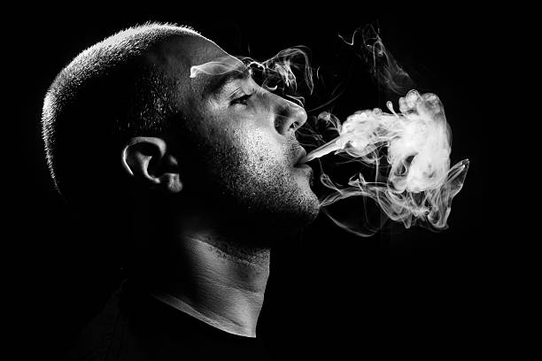 Smoking dark and sullen shot of a young man smoking over a black background smoking issues photos stock pictures, royalty-free photos & images