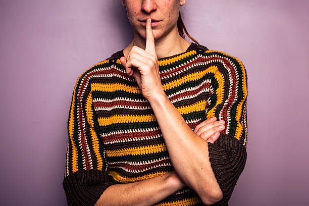 istock Young woman gesturing hush with her finger on lip 453820939