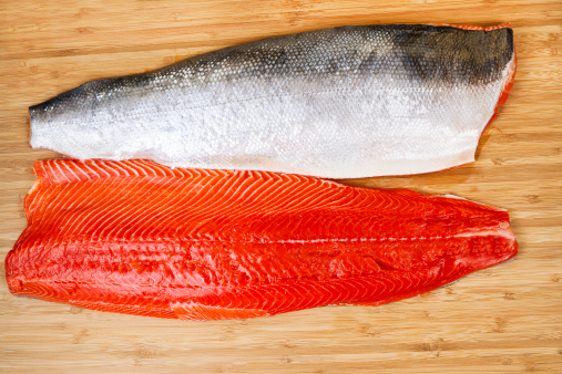 Horizontal photo of two Red Salmon fillets, one skin side up, on natural bamboo cutting board