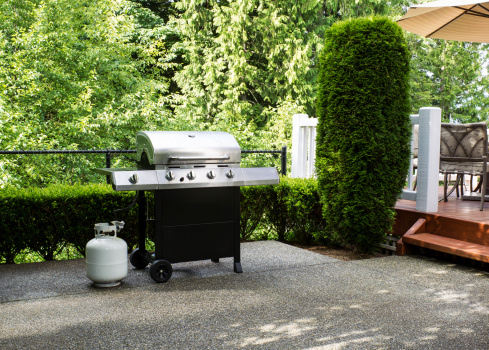 BBQ grill in a backyard with green grass and brick fence