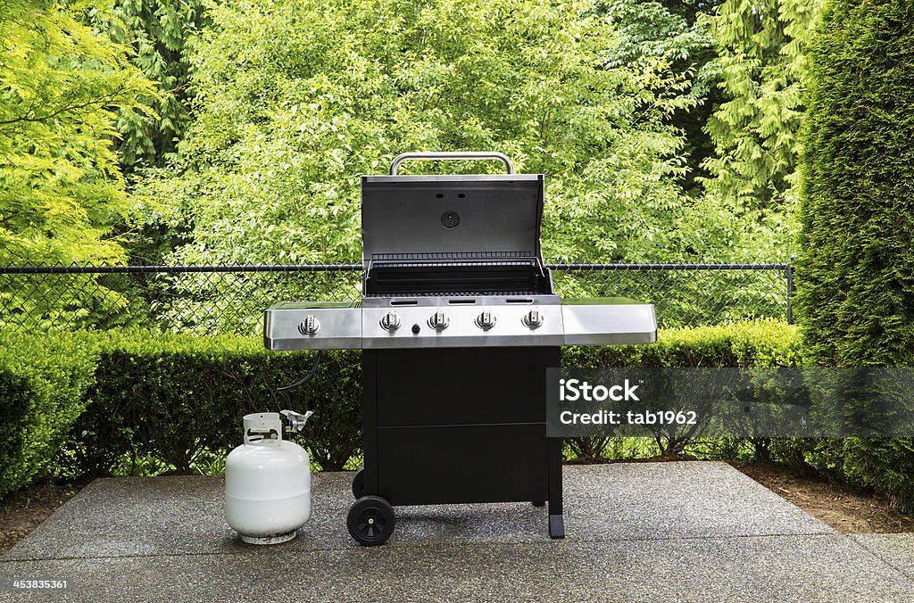 Gas grill with white tank on outdoor patio Horizontal photo of large barbeque cooker, with lid up, on concrete outdoor patio with woods background Barbecue Grill Stock Photo