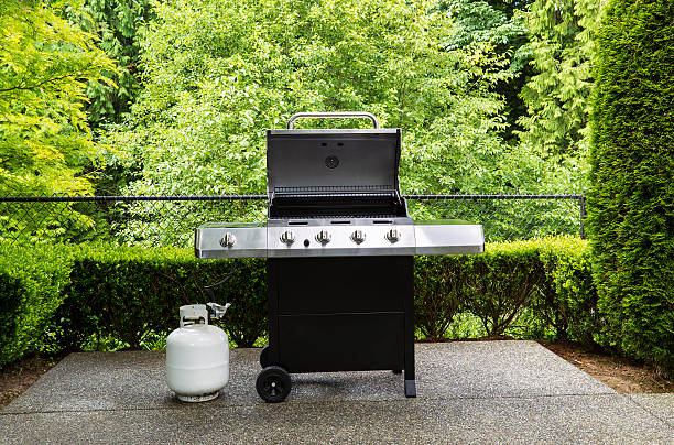 Gas grill with white tank on outdoor patio Horizontal photo of large barbeque cooker, with lid up, on concrete outdoor patio with woods background camping stove photos stock pictures, royalty-free photos & images