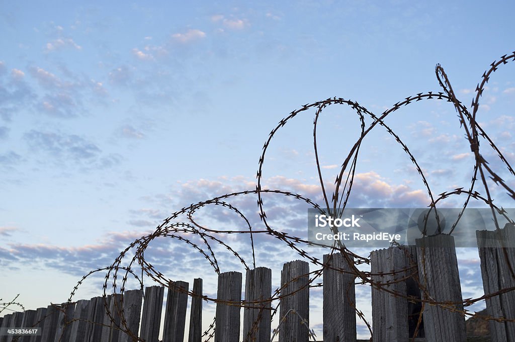 Rusty alambre afilado encimeras valla; Cielo azul detrás de las promesas de la libertad - Foto de stock de Afilado libre de derechos
