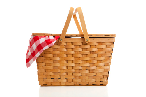 A brown wicker picnic basket on a white background with gingham cloth