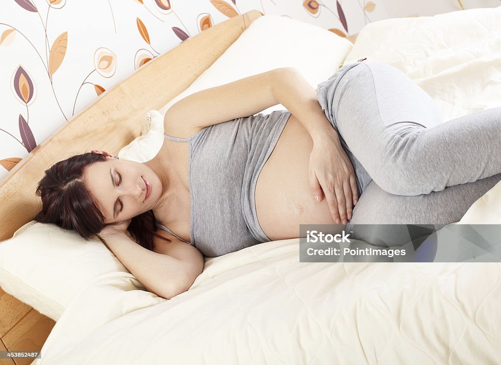 Pregnant woman lying in bed Pregnant woman lying in bed looking and holding her belly. 20-29 Years Stock Photo