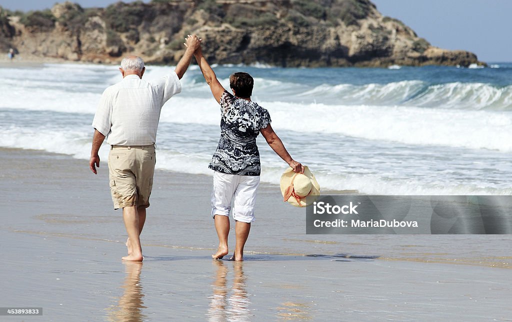 Happy senior couple walking together on a beach Happy elderly couple enjoying their retirement vacation near the sea 60-69 Years Stock Photo