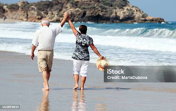 Happy Senior Couple Walking Together On A Beach Stock Photo - Download Image Now - 60-69 Years, Active Lifestyle, Active Seniors