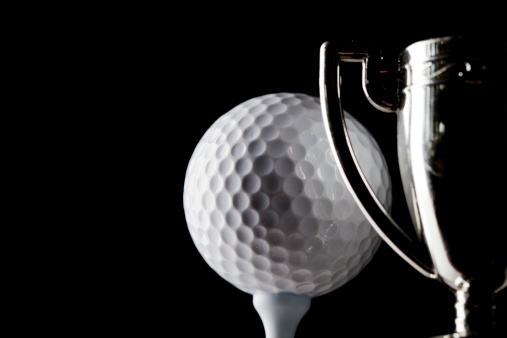 Golf ball and winners trophy against black background