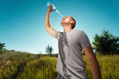 Young man is refreshing himself with water from the bottle after workout in nature.  Grain added to create atmosphere