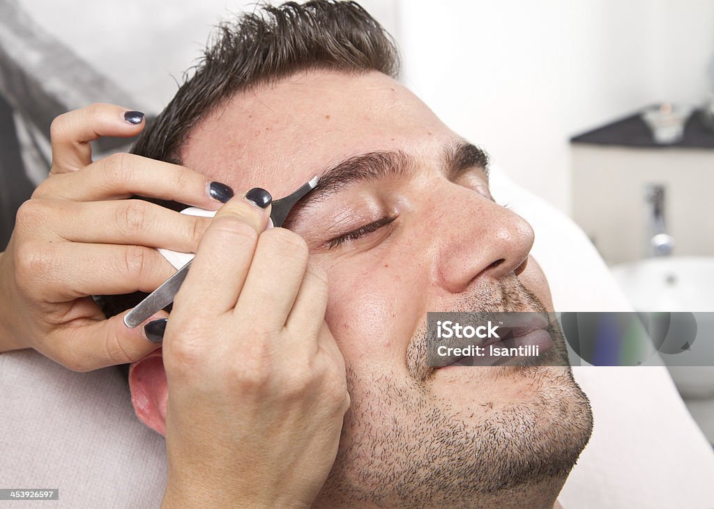 Beautician plucking a beautiful man eyebrows with tweezers a Beautician plucking a beautiful man eyebrows with tweezers in a beauty salon Adult Stock Photo