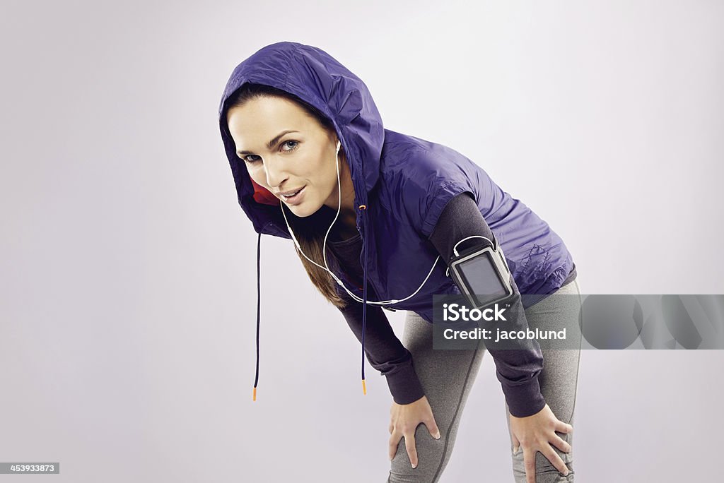 Pretty young woman takes a break after running Pretty young woman takes a break after running looking at camera smiling. Female runner looking tired over grey background 20-24 Years Stock Photo