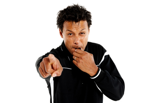 Portrait of soccer referee pointing at you and blowing a whistle against white background