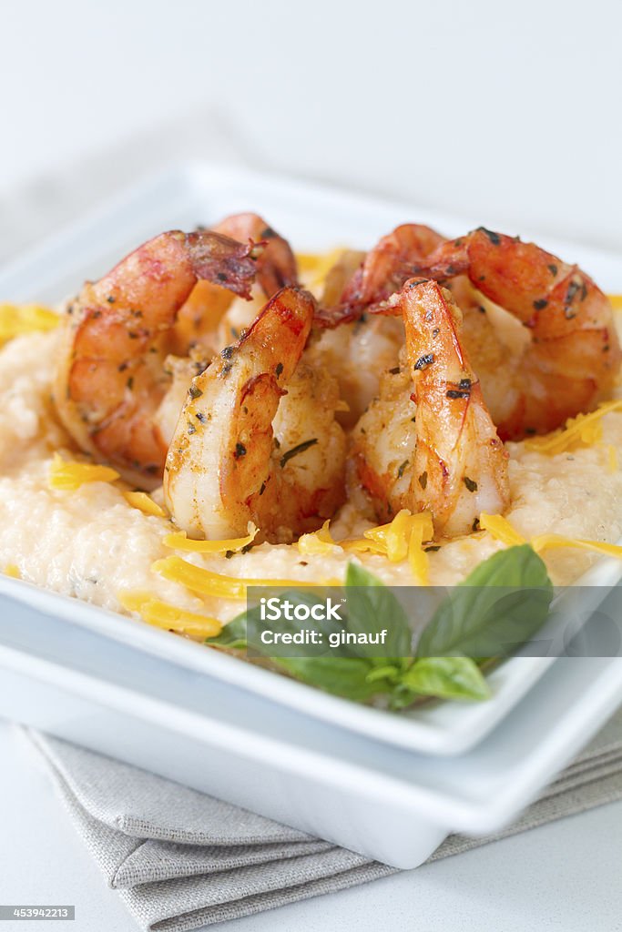 Cheesy Shrimp and grits_plain background A photo of sautéed shrimp served over cheesy grits.  The shrimp are cooked with butter, garlic, and herbs, the grits are boiled in chicken stock and blended with cheddar and cream cheeses, and the dish is garnished with a sprig of fresh basil.  A refreshing twist on southern cuisine. Basil Stock Photo