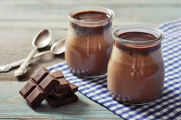 Chocolate dessert panna cotta in glass jars on wooden background