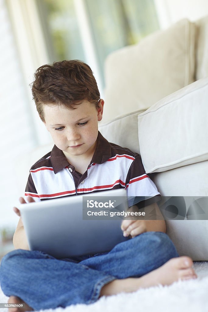 Engrossed in the wonders of online learning A cute little boy using a digital tablet while sitting at home 6-7 Years Stock Photo