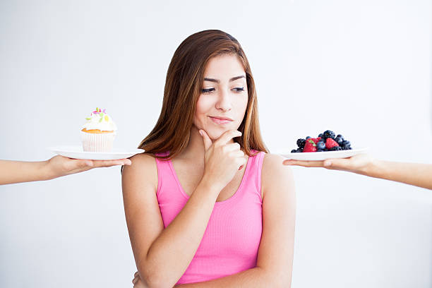 Smiling slim young caucasian woman in sportswear with donut in hand throws up green apple, has fun, isolated on blue studio background. Diet, choice of sweets or fruit, body care, weight loss