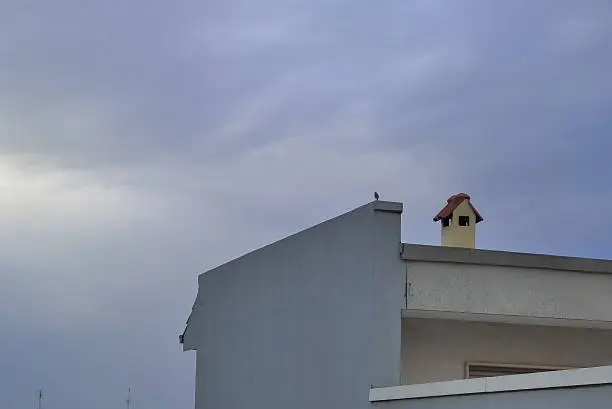 Photo of Cloudy sky with sparrow on roof.