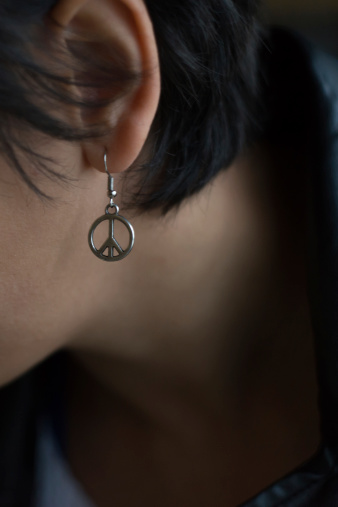Peace earring on a girls ear with short dark hair.