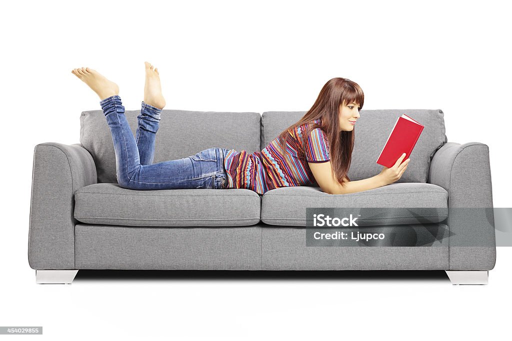 Young female lying on sofa and reading a book Young female lying on a sofa and reading a book isolated on white background Adult Stock Photo