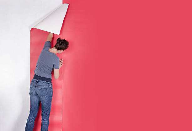 Woman wallpapering her house with red wallpaper. Decorating.