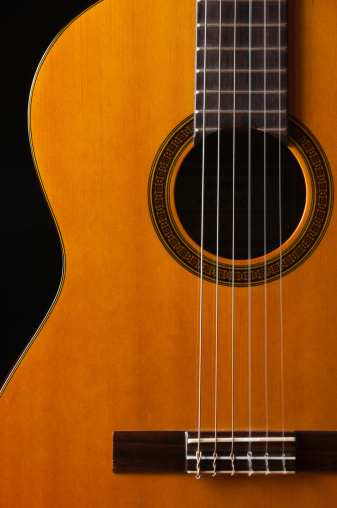 A close up image of a classical guitar with nylon strings isolated on a black background.