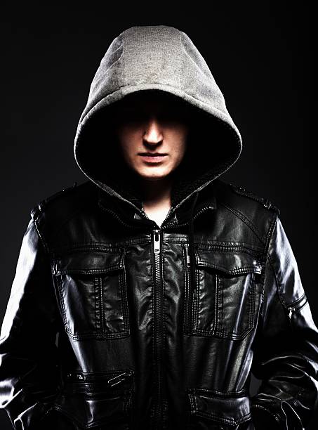 Scary hooligan man in leather jacket with a hood Scary hooligan man in leather jacket with a hood darkness background larrikin stock pictures, royalty-free photos & images
