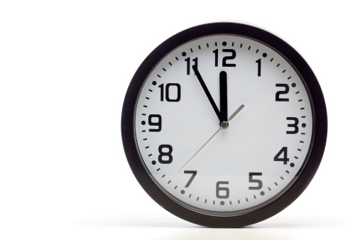 Analog clock with black frame, showing 5 to 12 - running out of time shortly.  Cutout, studio shot, isolated on white background.
