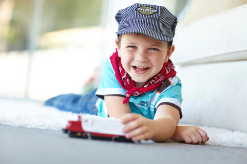 A cute little boy lying on the livingroom floor and playing with a toy train