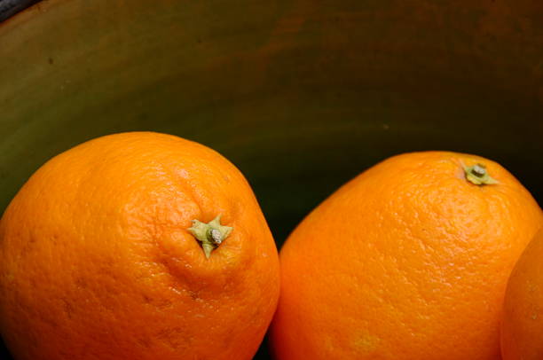 Two oranges fruits  in a green earthenware bowl