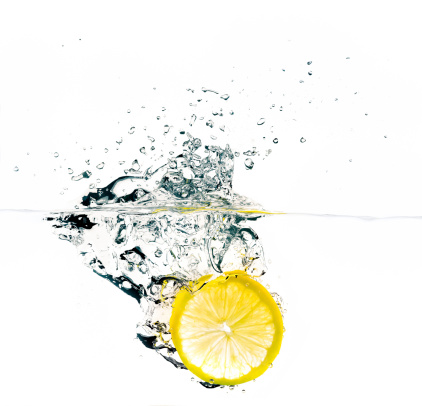 Bright lemon slice falling into water. Refreshing and healthy.