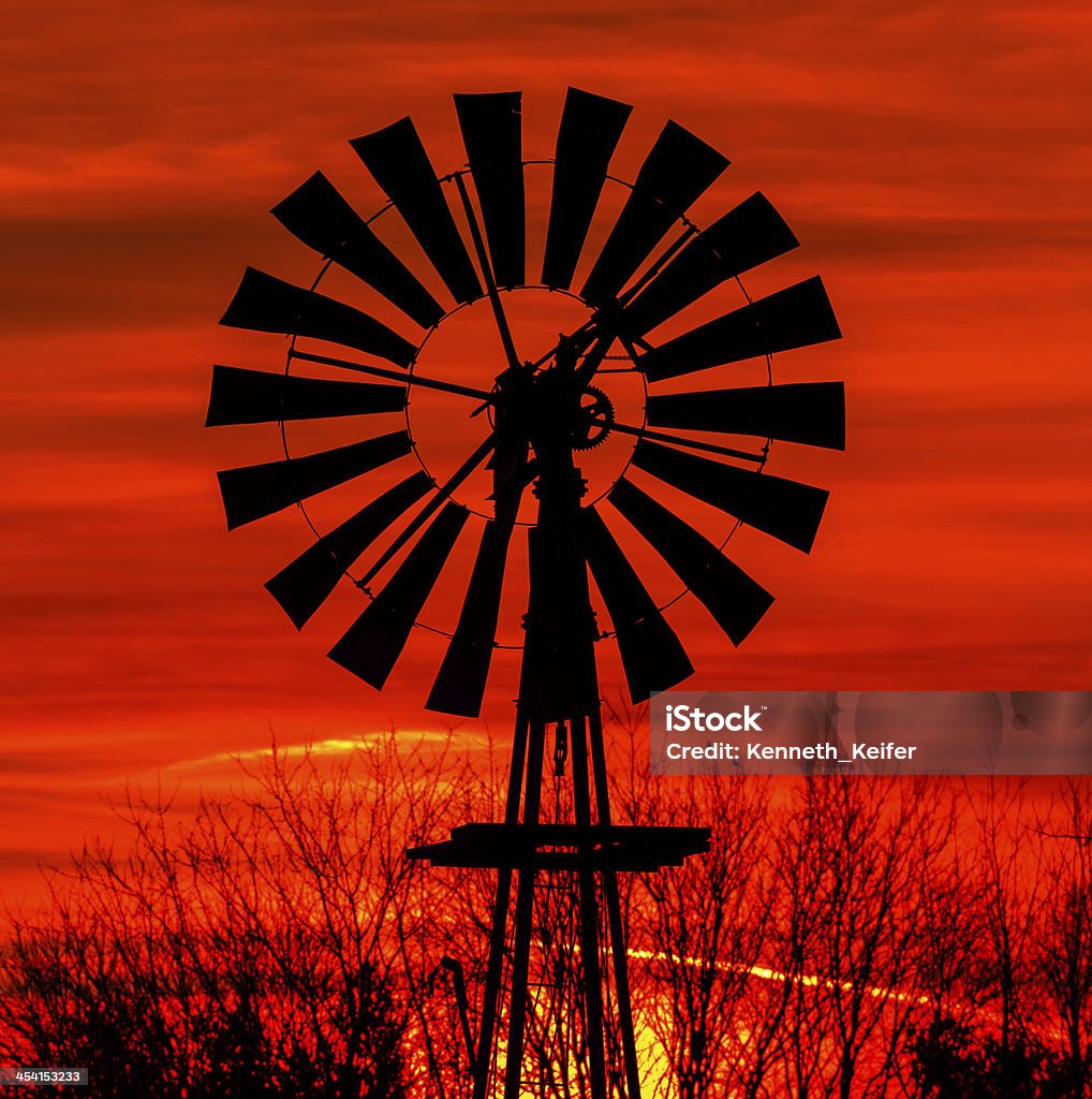 Antique windmill silhouetted by a colorful orange sky. Antique windmill is silhouetted by a colorful orange sky at sunrise in Indiana. Agricultural Machinery Stock Photo
