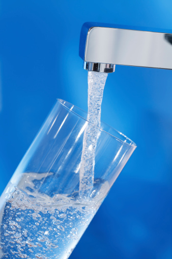 Filling up a glass of water . Blue background.