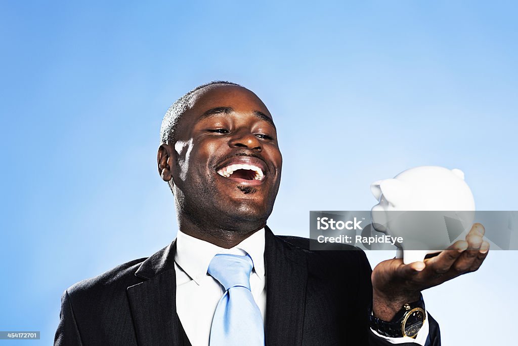 My savings plan is looking good! Laughing busnessman with piggybank An African-American man in formal business wear gives a beaming smile as he considers a white piggybank he is holding.  His savings plan is going very well indeed! 30-39 Years Stock Photo