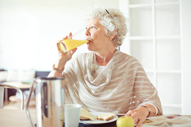 anziani donna bere succo d'arancia - women juice drinking breakfast foto e immagini stock