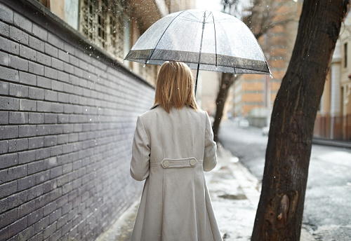Rearview shot of a woman walking down a street in the rain and holding an umbrella