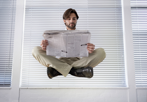 A young businessman levitating while reading a newspaper