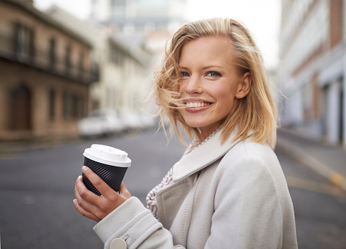 Head and shoulders portrait of a young woman walking in the street with a cup of coffee