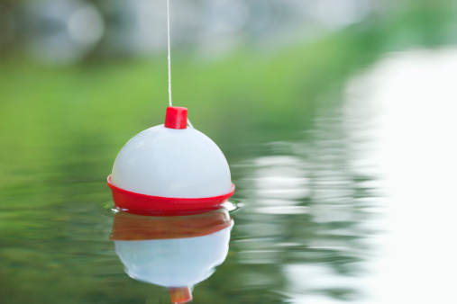 A red and white bobber floats on water with ripples
