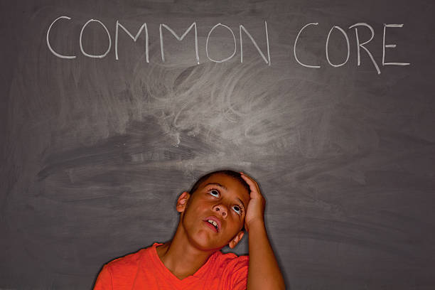 Elementary age boy in front of chalkboard with "common core" stock photo