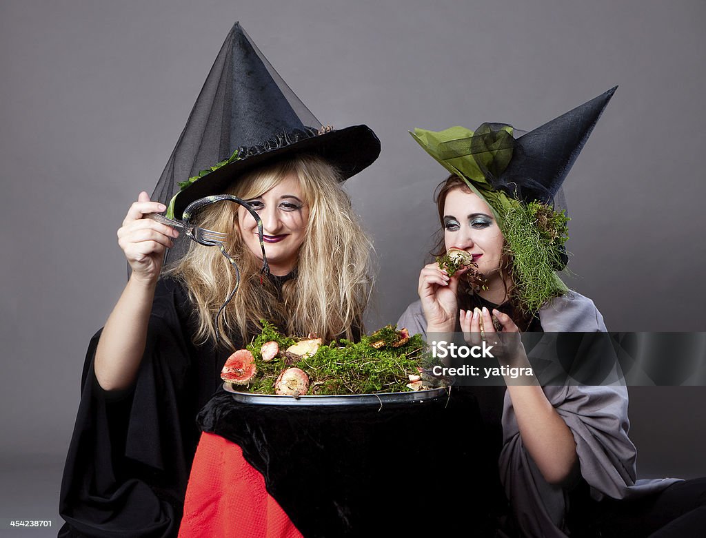 Halloween party - girls in costumes of witches Halloween party - girls in costumes of witches dine snakes and mushrooms Adult Stock Photo