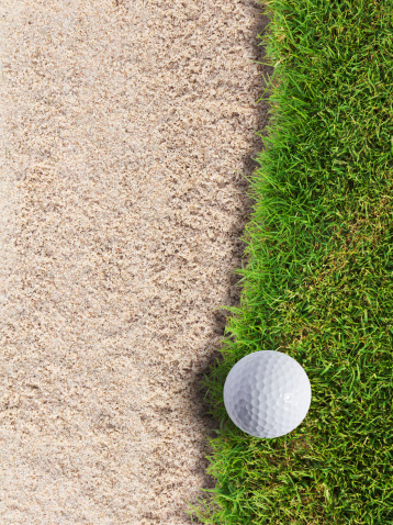 Golf ball on green grass near sand bunker