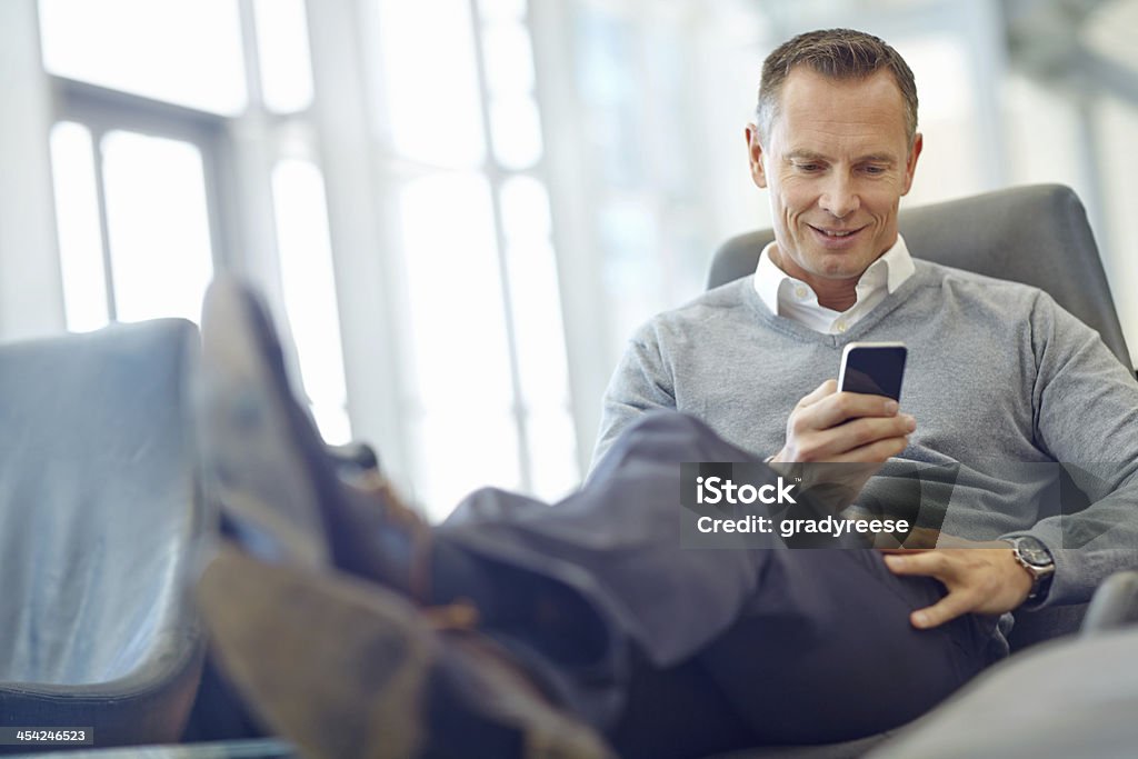 Sending an old client a friendly text Handsome mature businessman checking his mobile while relaxing Mature Men Stock Photo